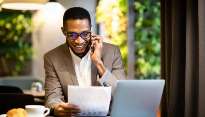 Business, Technology And Communication Concept. Afro manager making phone call while looking at document with graphs